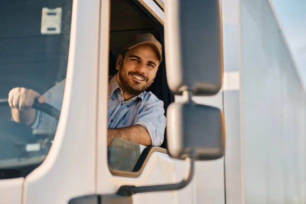 Driver smiling from the open window of a white truck cab