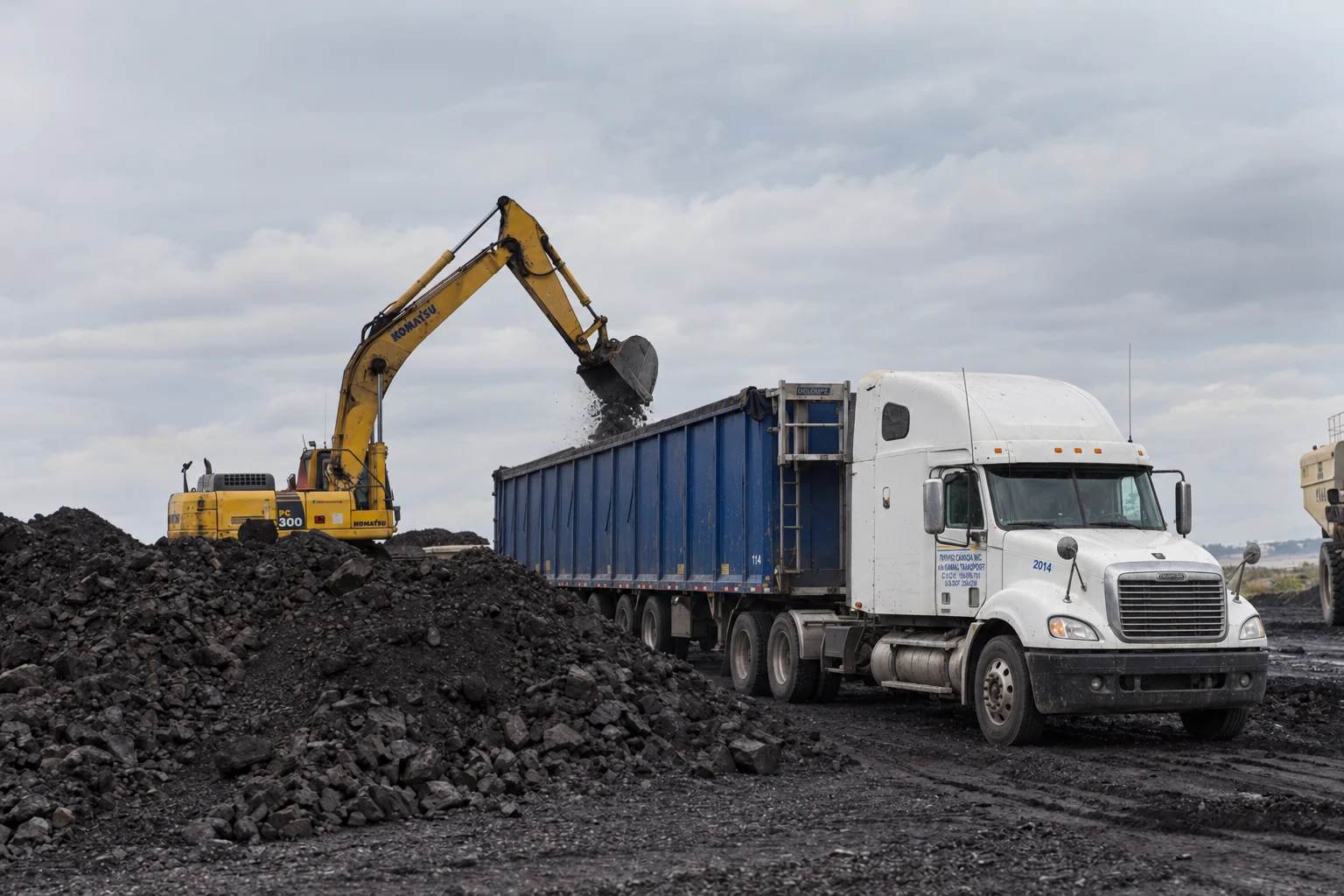 An excavator loading aggregate into a Kamal Transport blue trailer